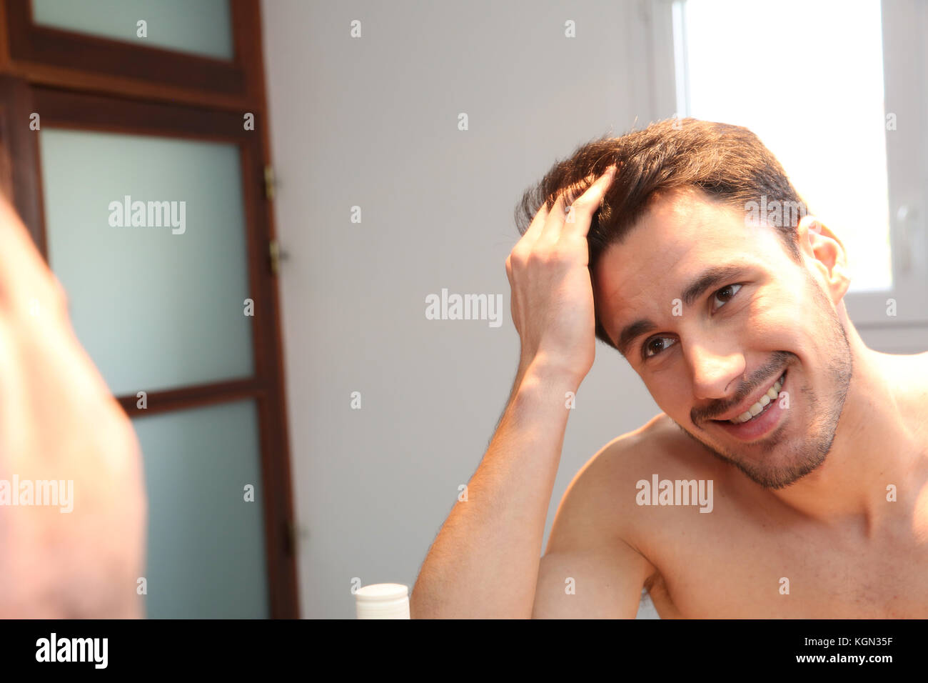 Young man looking at hair in mirror Stock Photo