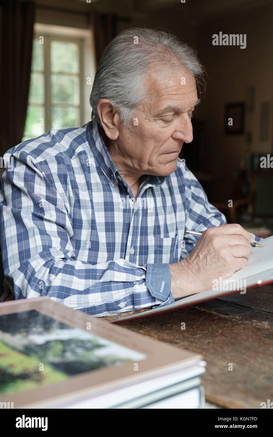 Senior man at home relaxing and writing on notebook Stock Photo