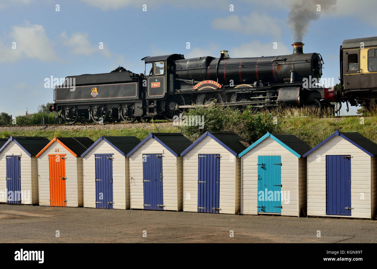 Steam train passing beach huts at Goodrington Sands, hauled by GWR loco No 7827 Lydham Manor. Stock Photo