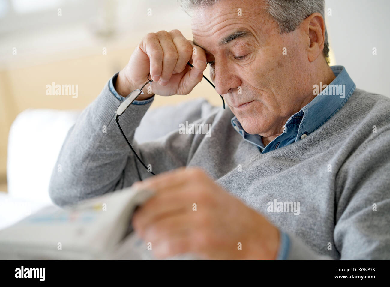 Senior man having a headache reading newspaper Stock Photo