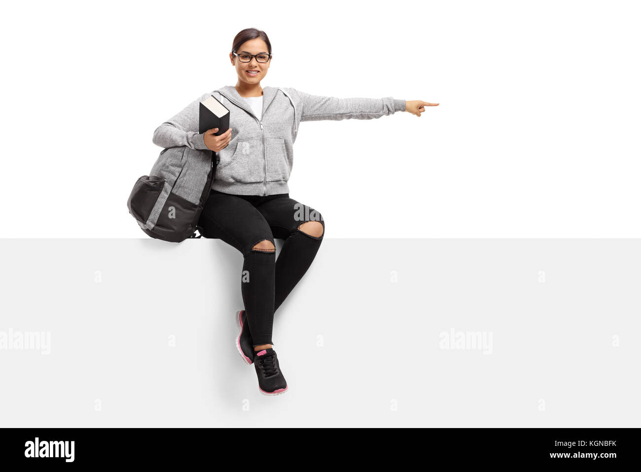 Cheerful teenage student with a backpack and a book sitting on a panel ...
