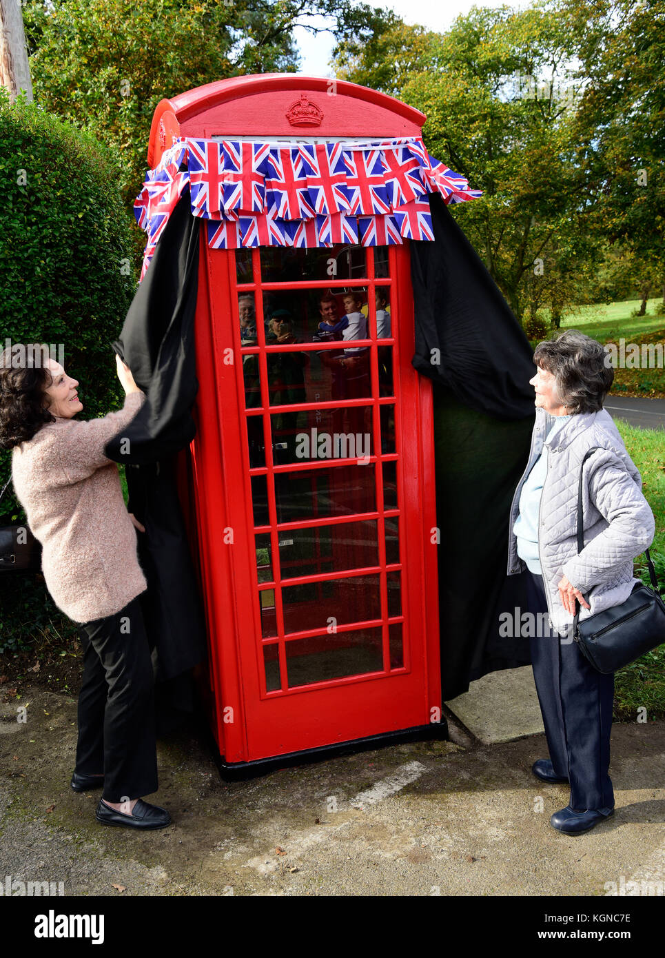 Two elderly residents of the village of Frensham unveil a renovated, traditional red  phone box which has been converted into a small visitors centre. Stock Photo