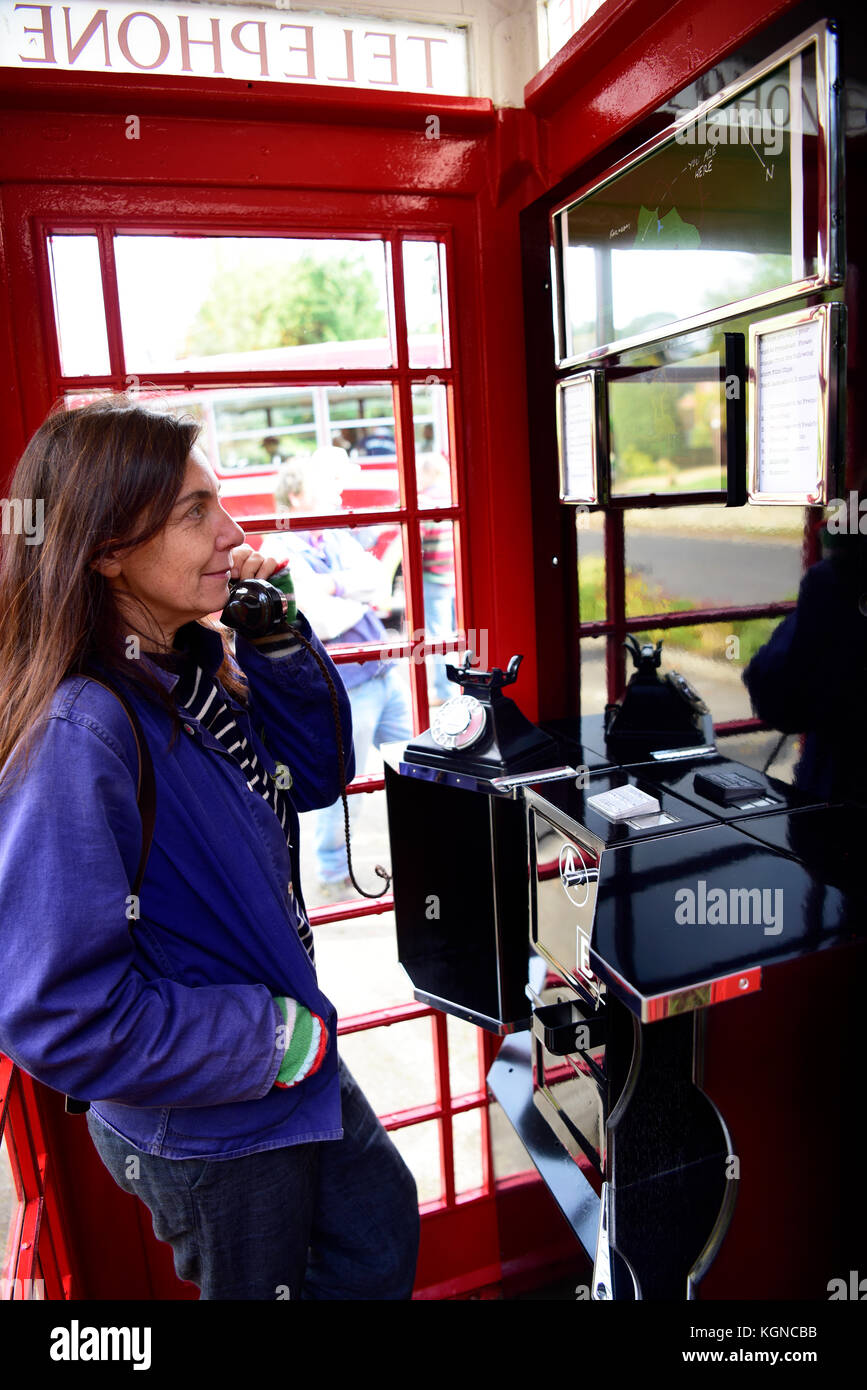 Female local resident using a traditional red phone box which has been converted into a small visitors centre. The interior of the phone box now has a Stock Photo