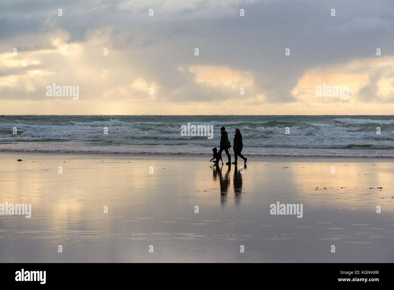 People walking along beach at sunset, Constantine Bay, St Merryn, Cornwall, November, with reflection in wet sand, UK Stock Photo