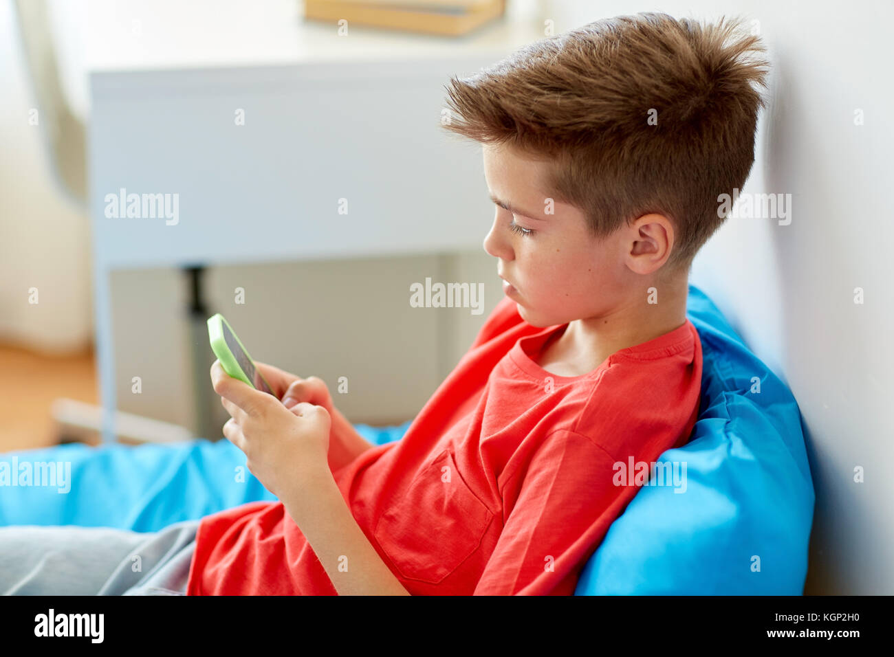 boy with smartphone lying on bed at home Stock Photo