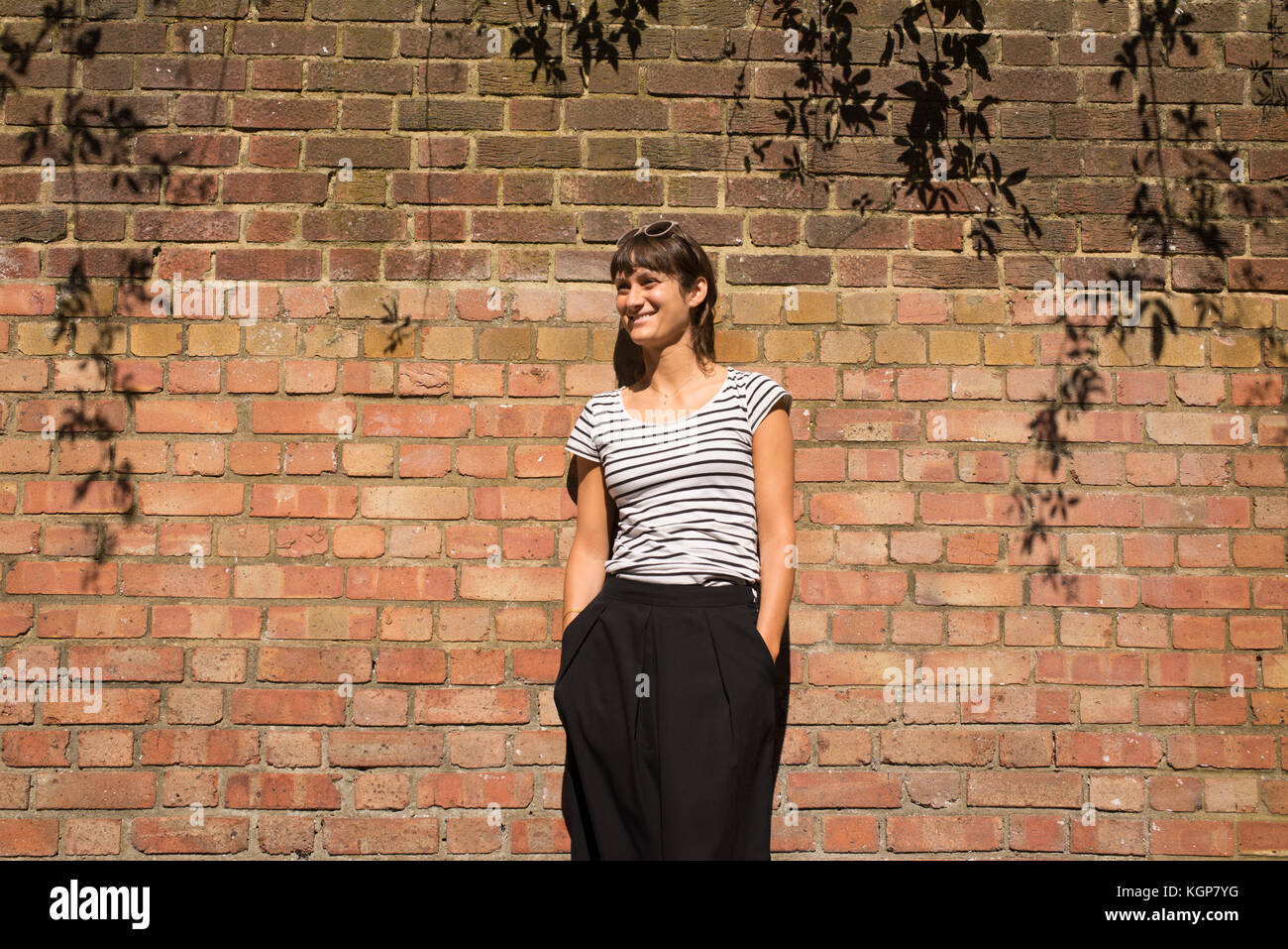 Young Woman dressed in urban minimal style with black and white striped T-shirt and black trousers. Brick wall as background Stock Photo