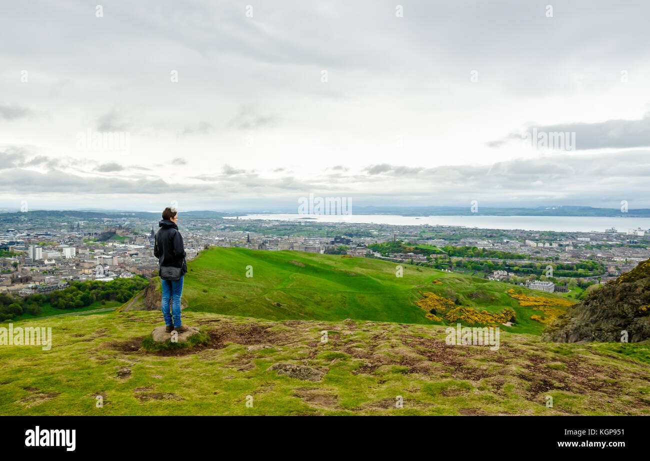 Young female model admiring Edinburgh landscape from the top of the Arthur's seat. Scotland, UK. Stock Photo