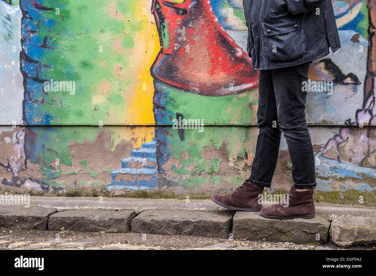 Model wearing tight black denim skinny trousers and brown suede ankle boots and walking in front of a graffiti wall. Focus on legs and shoes. Stock Photo