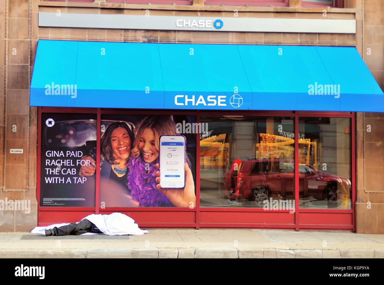 Social contrasts exist on a downtown Chicago street as a homeless man sleeps beneath a 'No Loitering' sign and a bank message. Chicago, Illinois, USA. Stock Photo