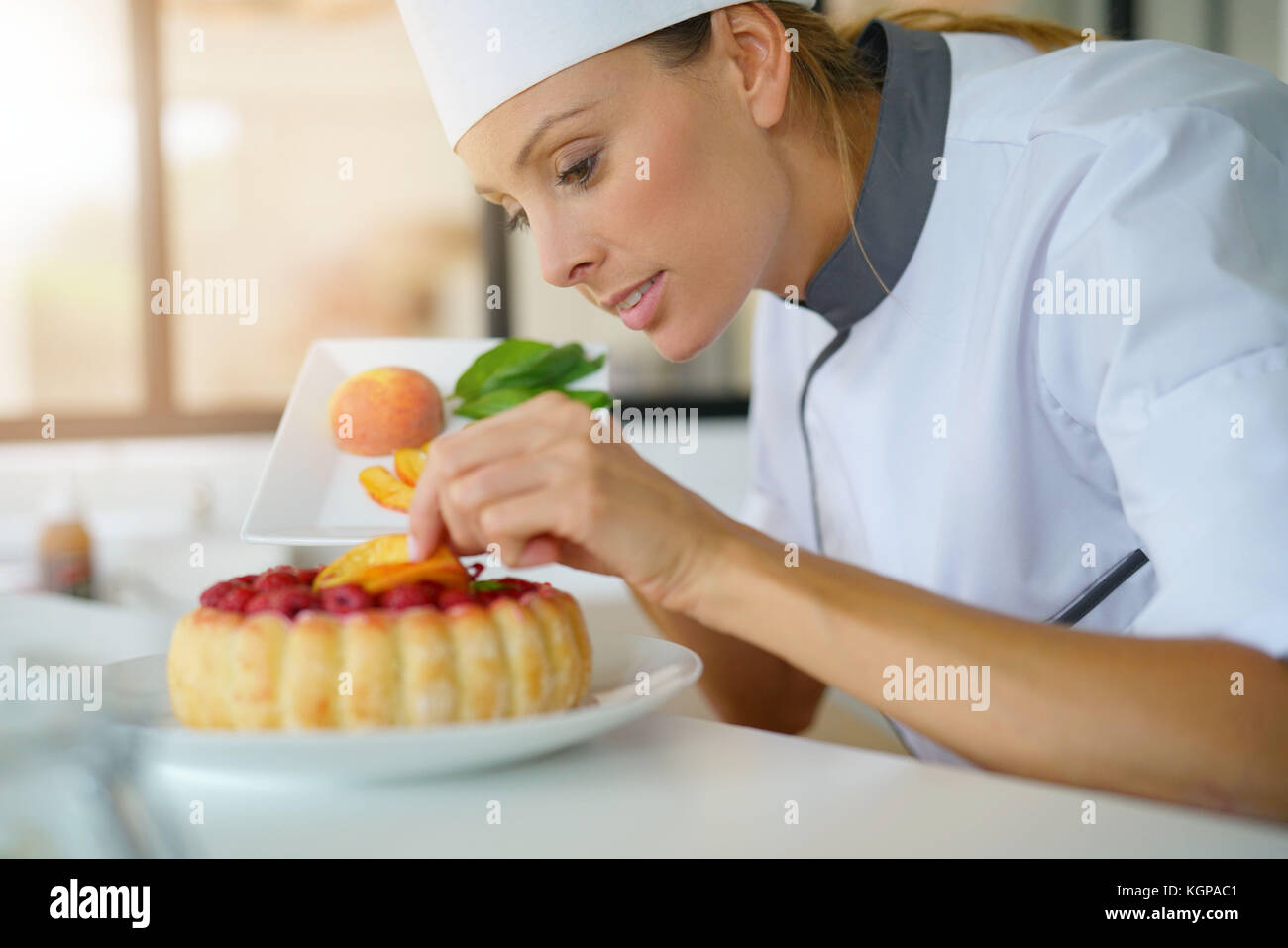 Pastry chef in professional kitchen decorating raspberry cake with fruits Stock Photo