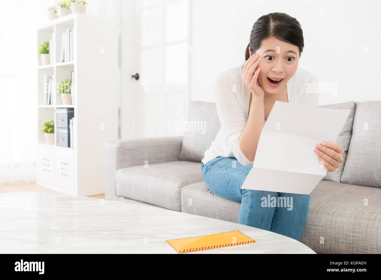 cheerful pretty female student received school admission notification letter feeling surprised when she sitting on sofa at home. Stock Photo