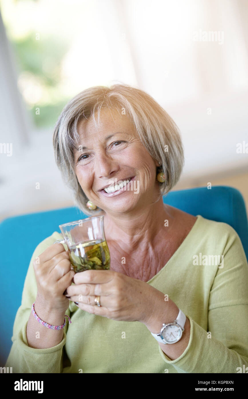 Senior woman relaxing in armchair drinking hot tea Stock Photo