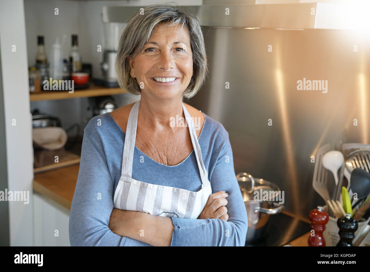 Cheerful Senior woman standing by stove in kitchen Stock Photo