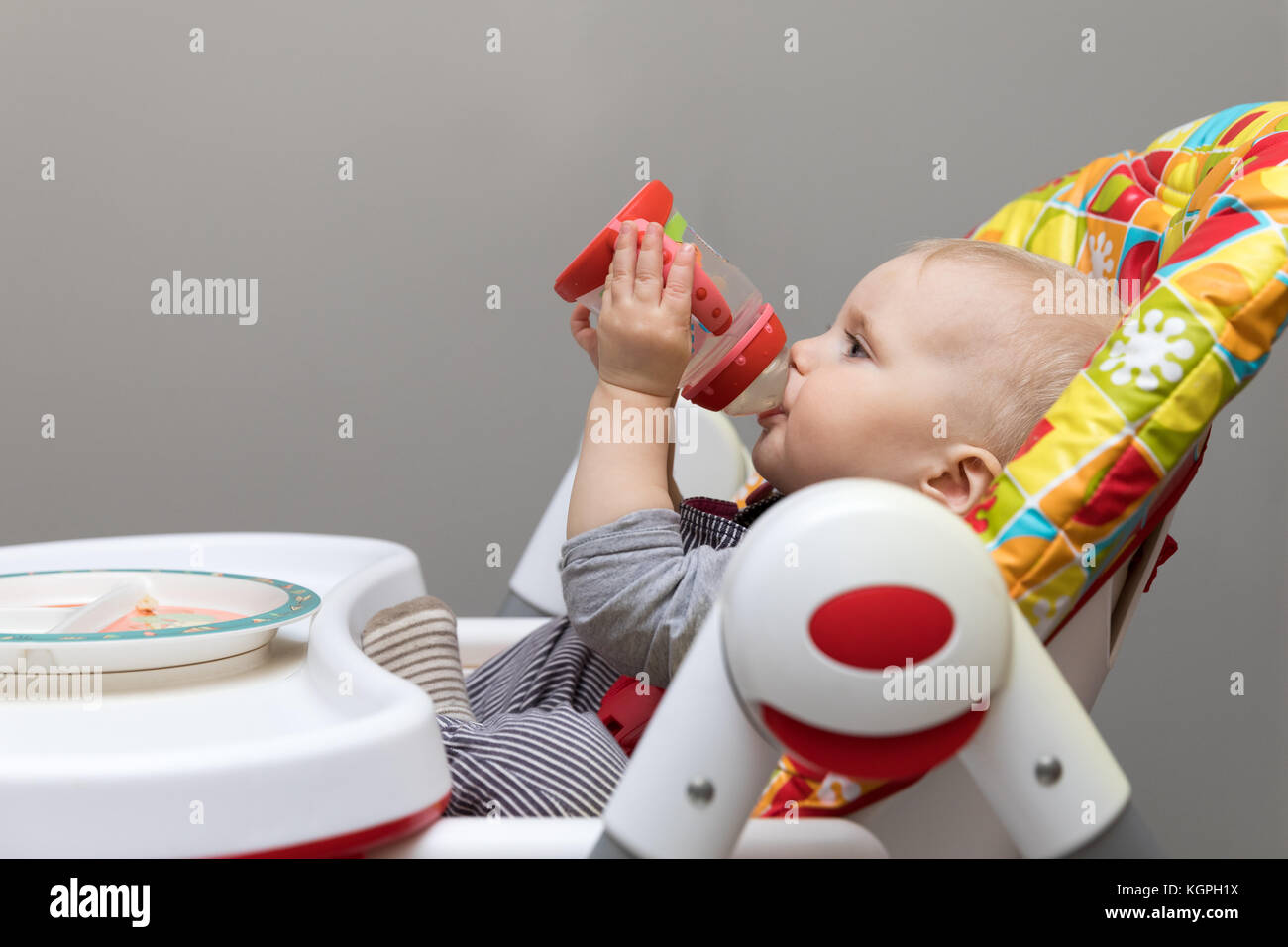 baby sitting in feeding chair and drinking water from bottle Stock Photo