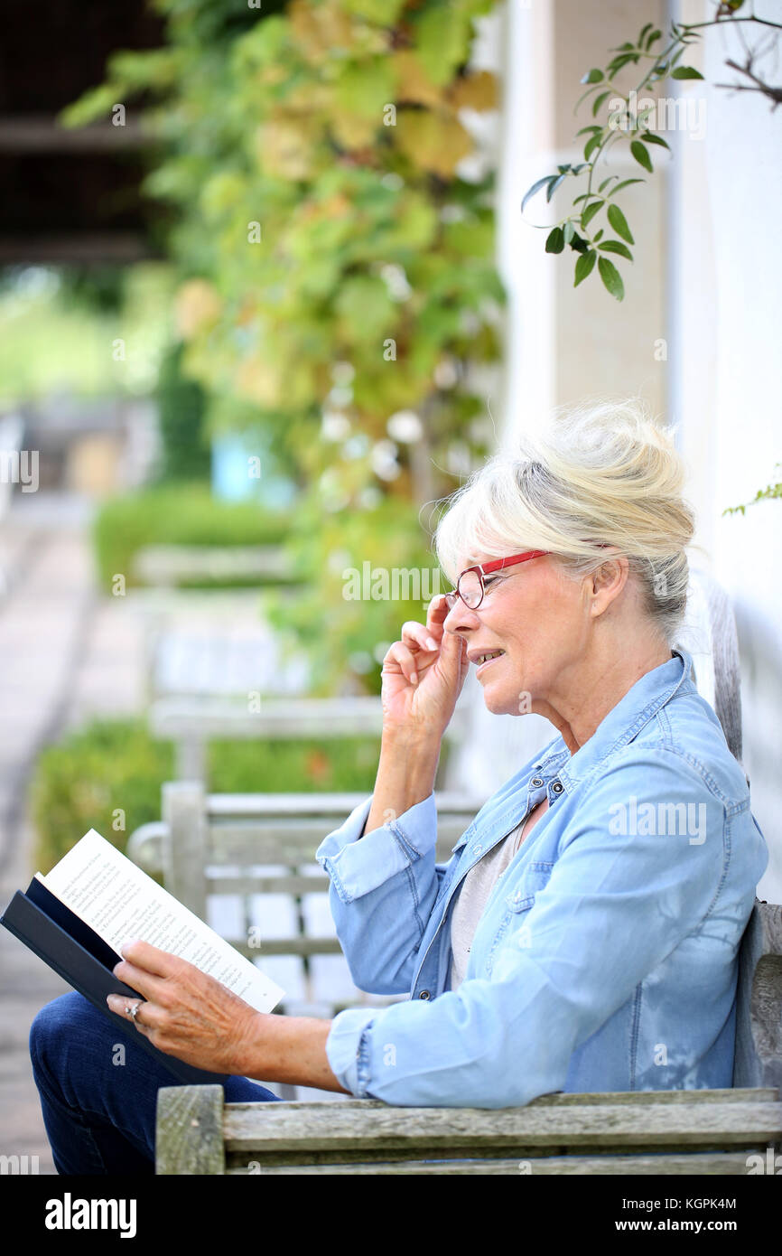 Senior woman reading book sit on bench Stock Photo - Alamy