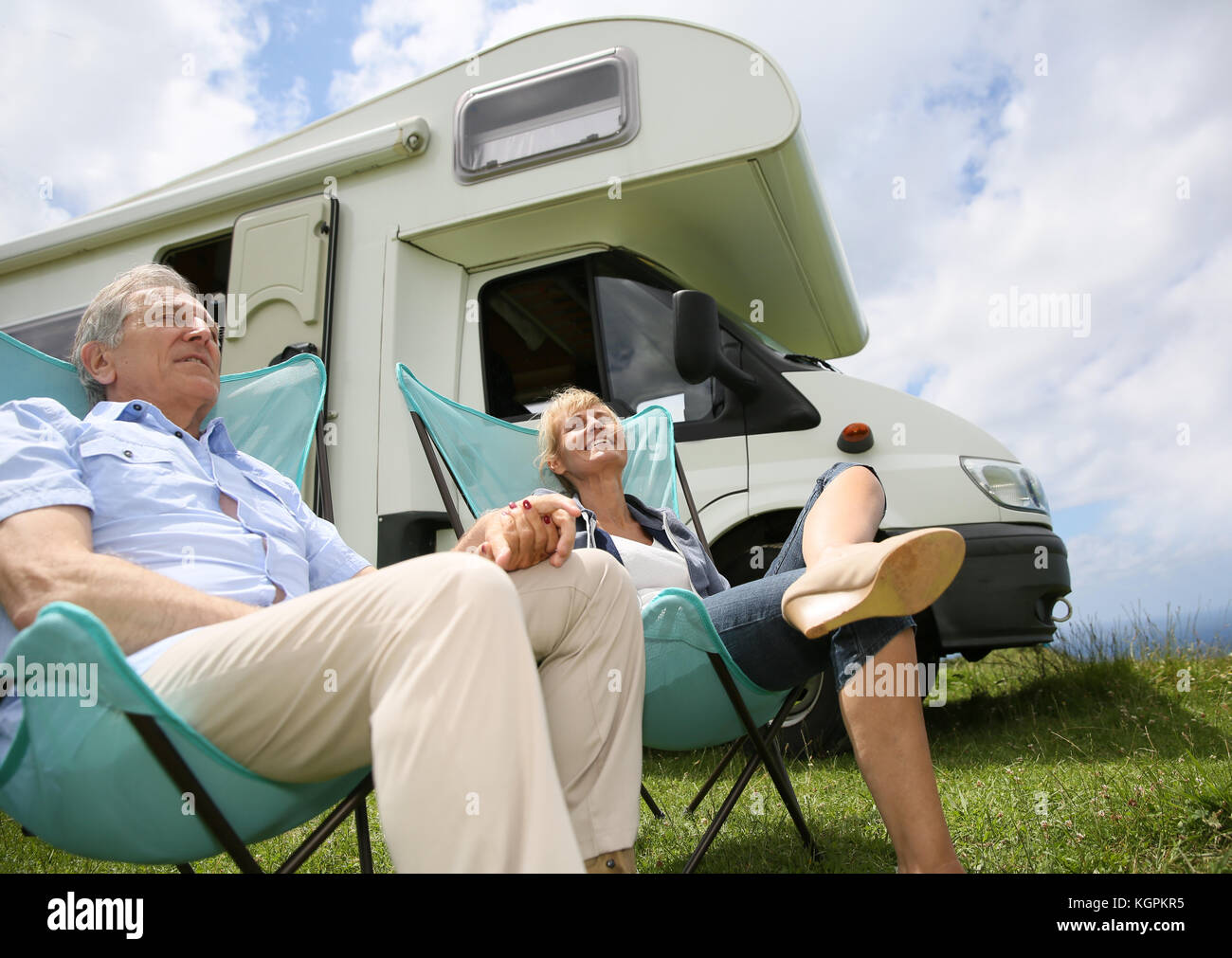 Senior couple relaxing in camping folding chairs, camper in background