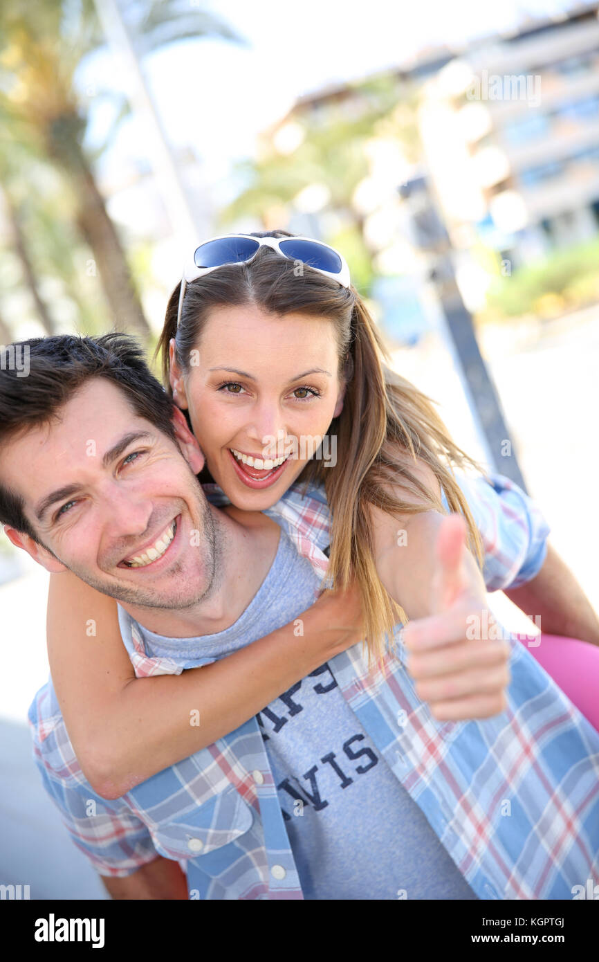 Cheerful girl on boyfriend's back showing thumbs up Stock Photo