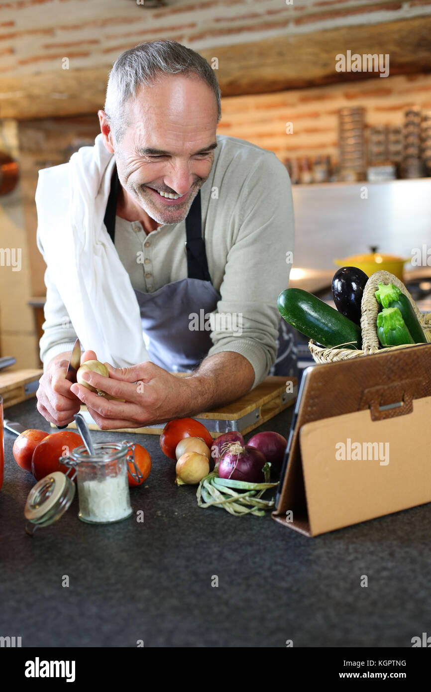 Mature man in kitchen reading recipe on tablet Stock Photo