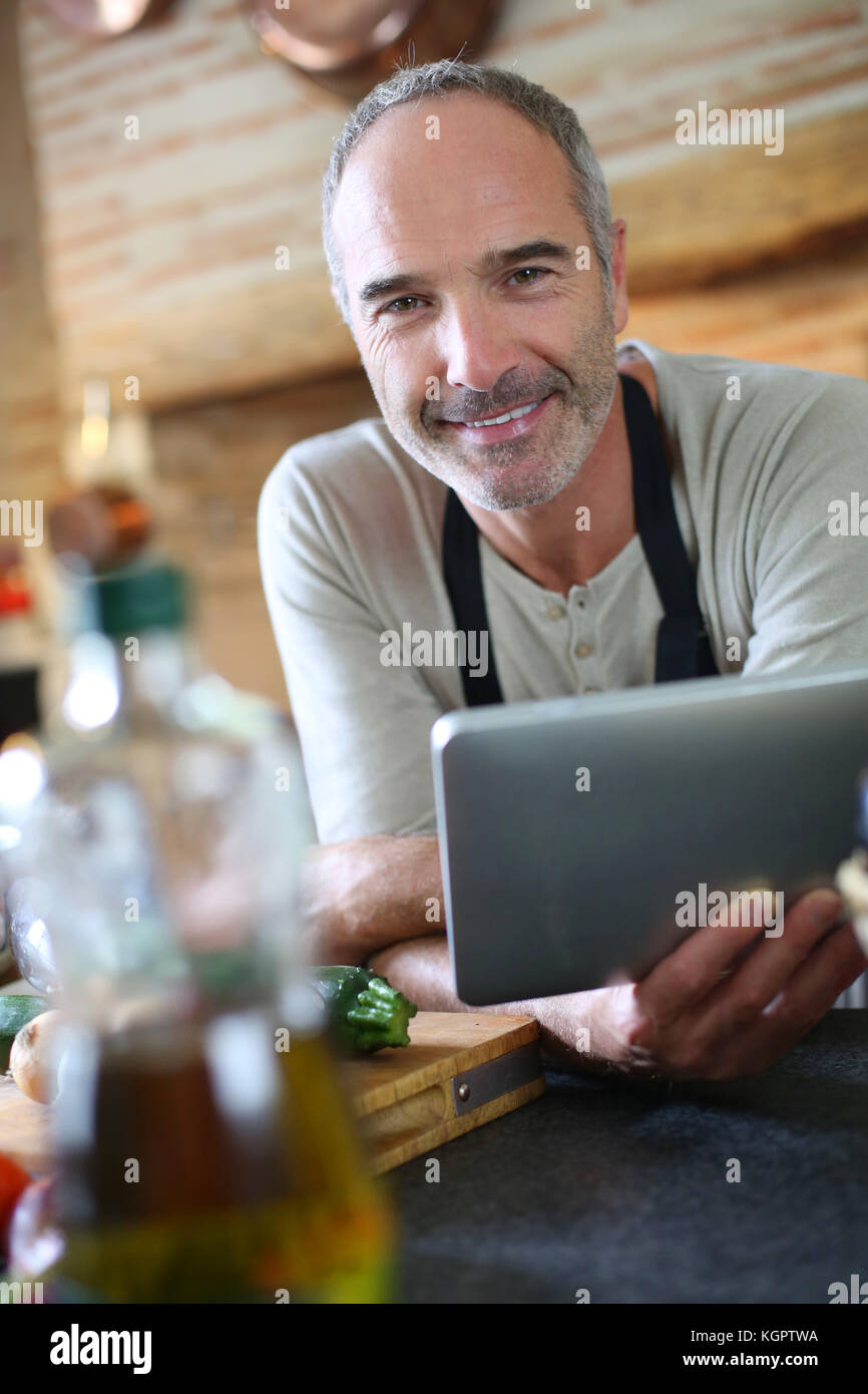 Mature man in kitchen reading recipe on tablet Stock Photo