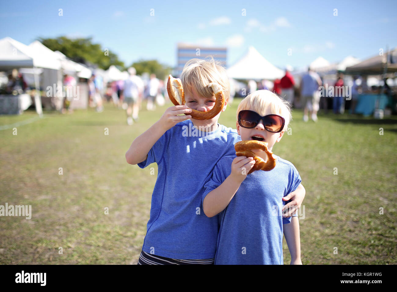 Two young boys: a seven year old and his little brother, are having fun eating pretzles and making funny faces at a farmer's market outside in Marco I Stock Photo