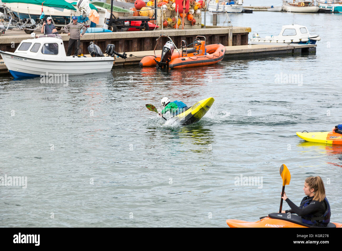 young kayakers training in Falmouth harbour, UK with quayside and boats in background. instructor demonstrating eskimo roll Stock Photo