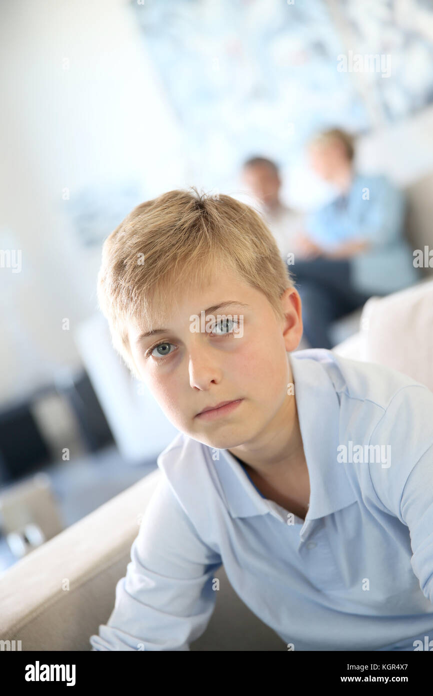 12-year-old boy sitting in couch at home, parents in background Stock Photo