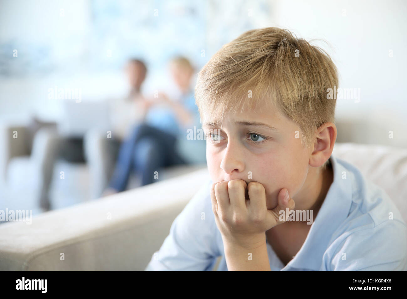 12-year-old boy sitting in couch at home, parents in background Stock Photo