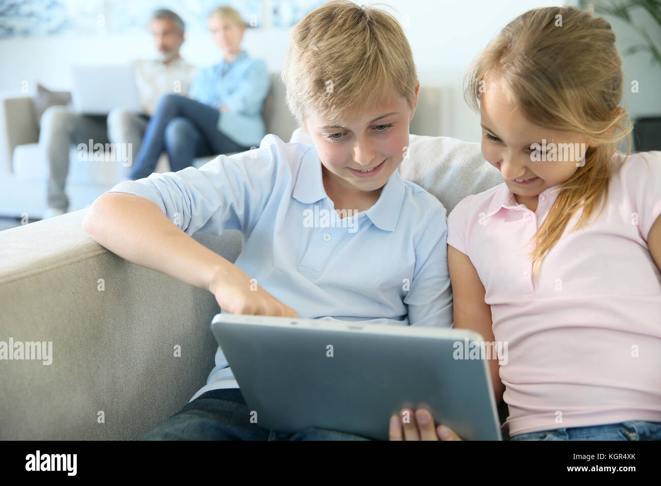Kids using digital tablet at home, parents in background Stock Photo ...