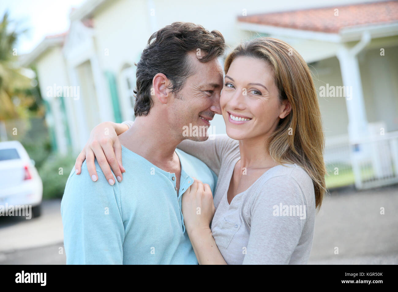 Cute loving couple standing in front of home and laughing Stock Photo ...