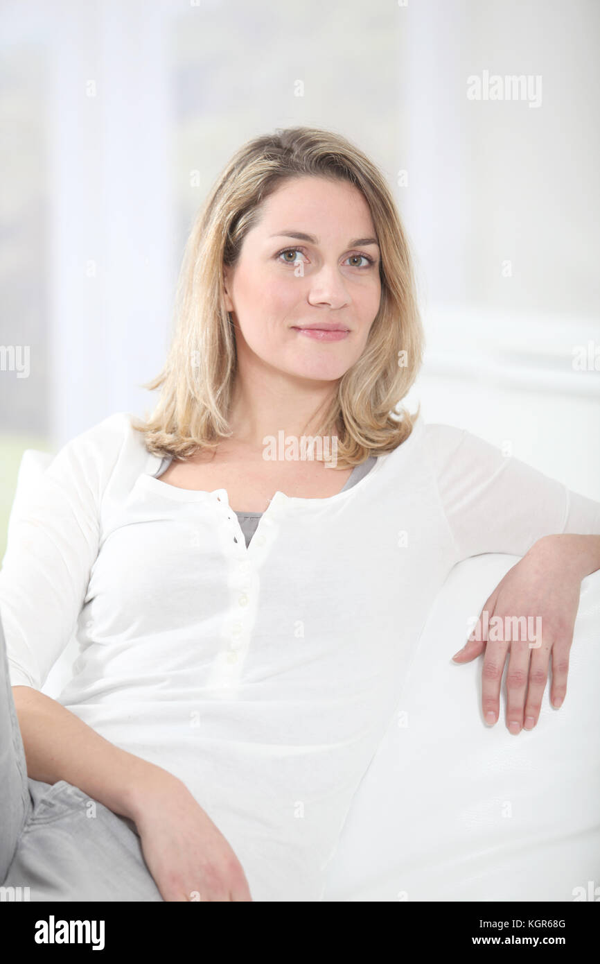 Portrait of beautiful blond woman sitting on sofa Stock Photo - Alamy