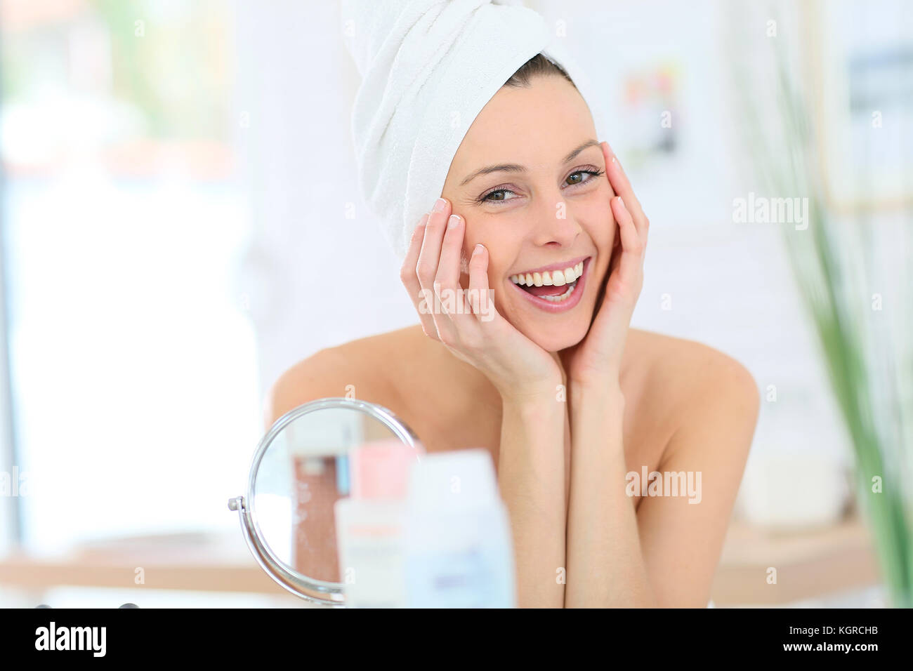 Cheerful woman in bathroom with towel over hair Stock Photo