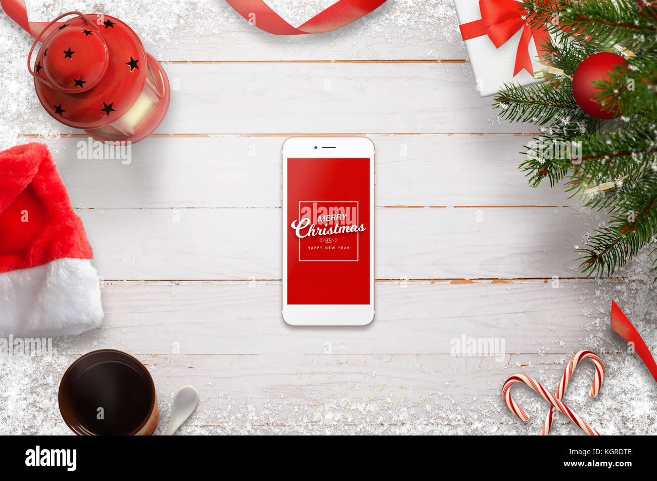 Hero header Christmas scene with mobile phone in the middle with Merry Christmas message. Christmas tree, gifts, decorations on white wooden desk. Stock Photo
