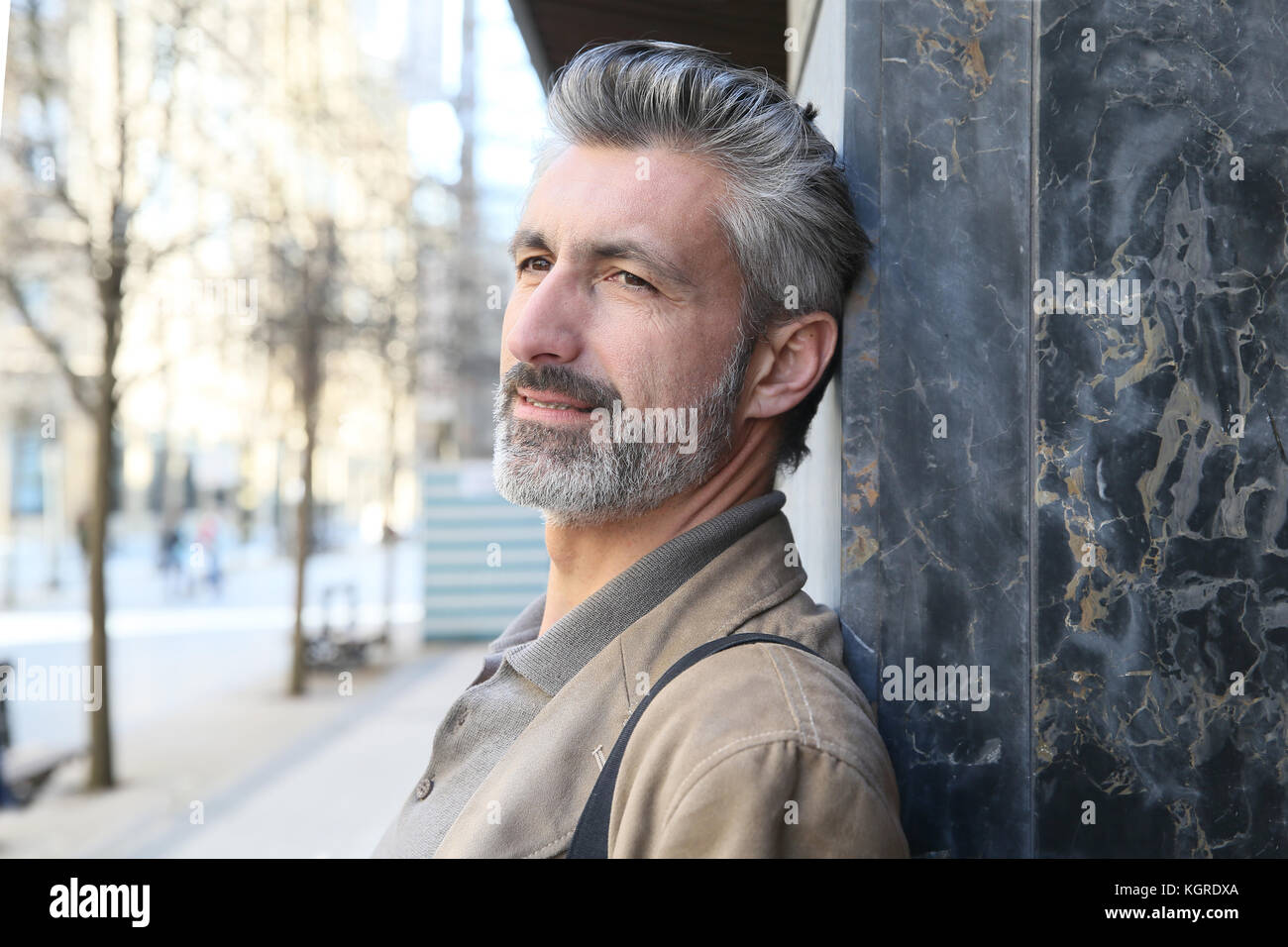 Mature man leaning on building wall in town Stock Photo