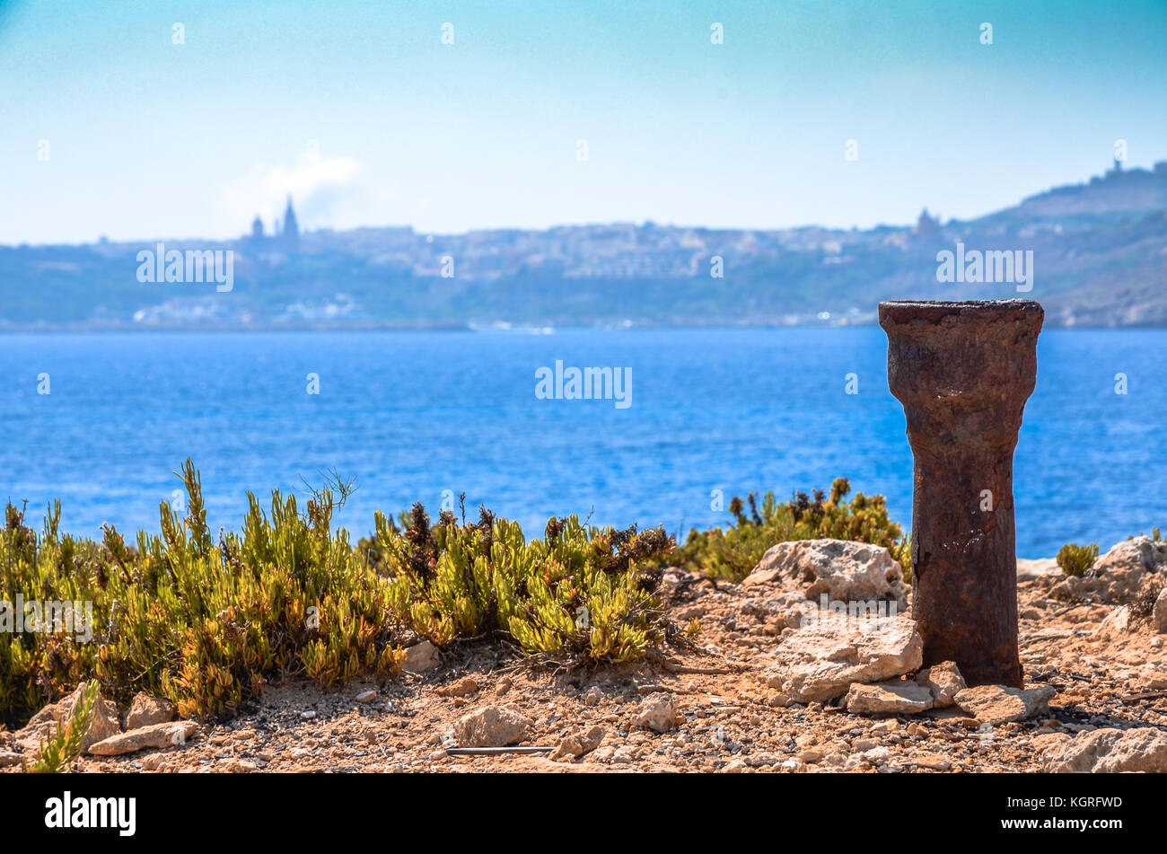 A rusting metal object on the Comino Island with Gozo in the background across the Mediterranean Sea in Malta Stock Photo