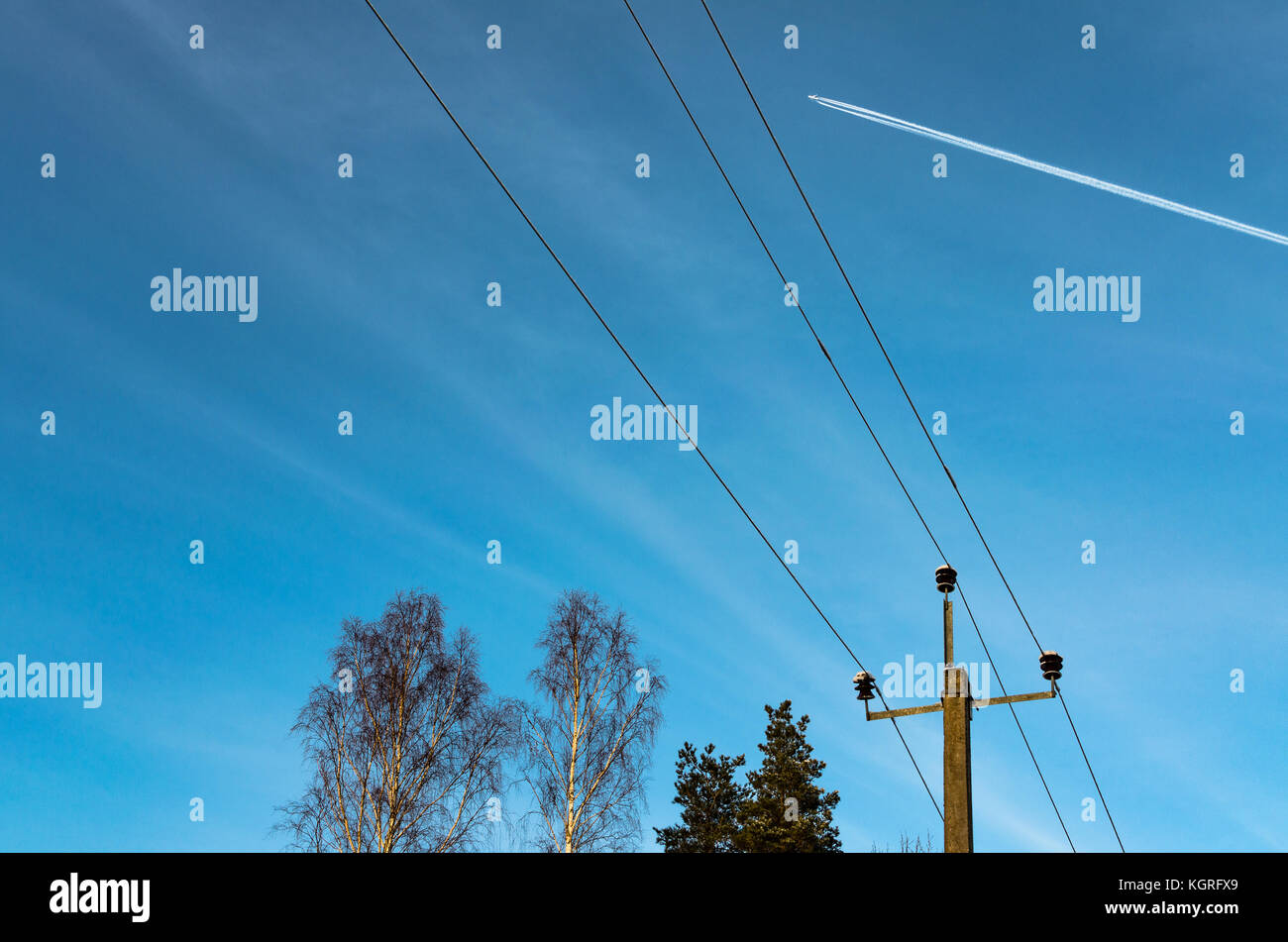 A plane in high flight and vapour trails above telephone lines Stock Photo