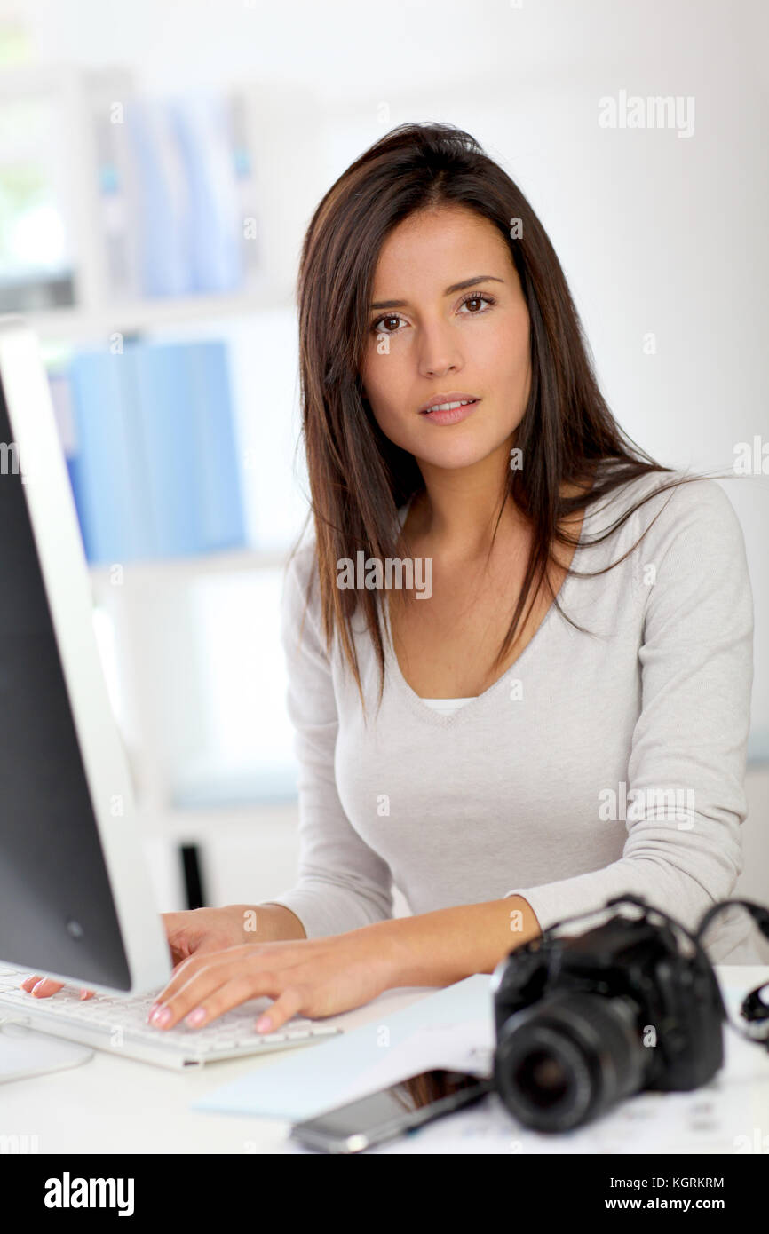Young woman photo reporter sitting in front of desktop computer Stock