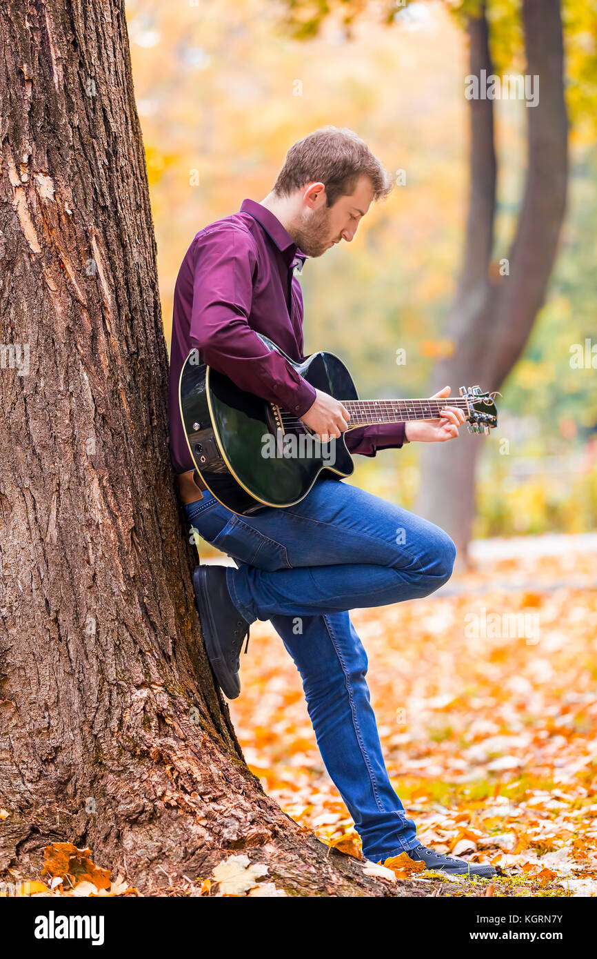 Young man playing acoustic guitar in city park. Focus on hand. Stock Photo