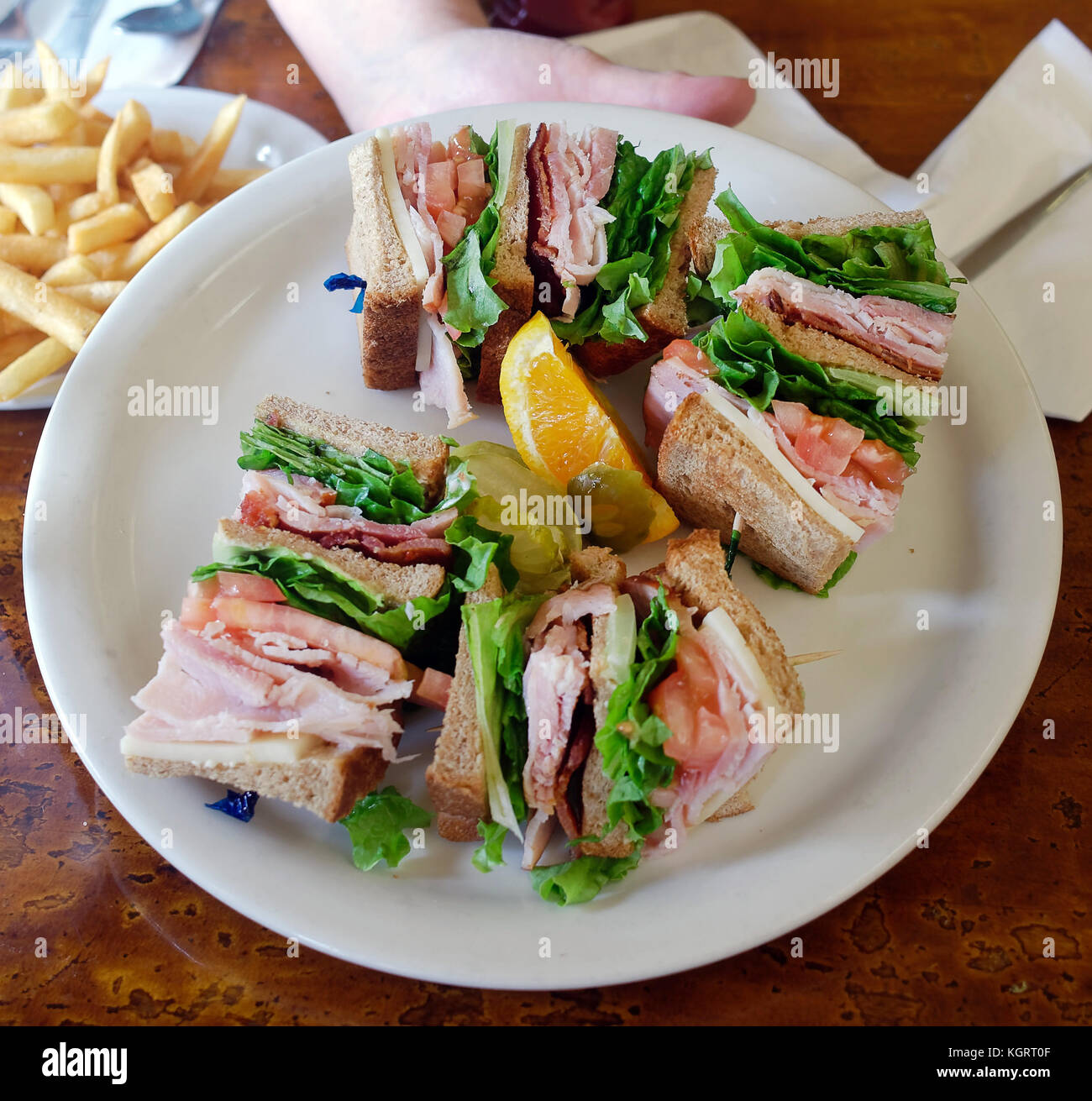 Hand presenting basic triangle cut club sandwich on white plate. Stock Photo