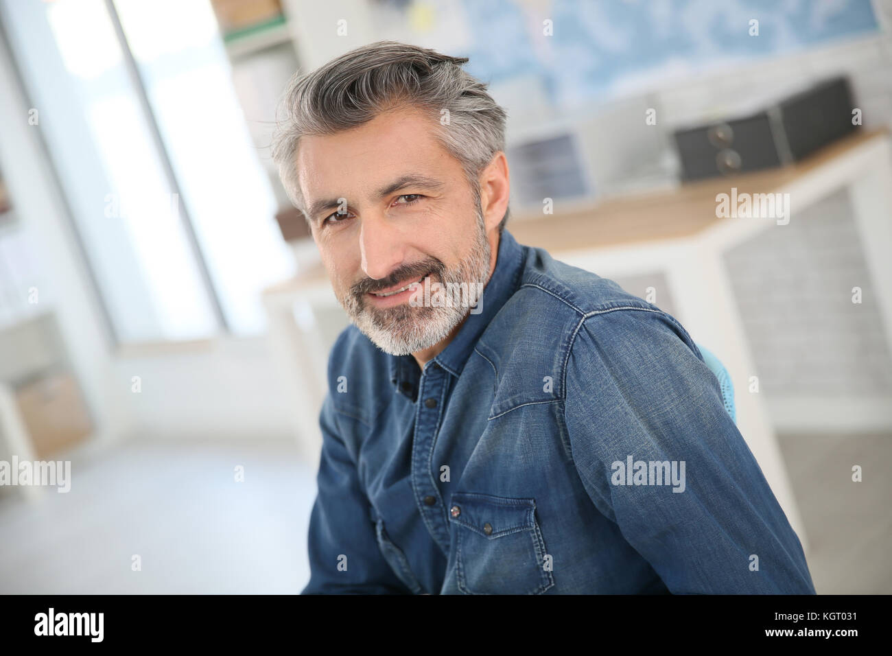 Smiling teacher sitting at desk in university office Stock Photo - Alamy