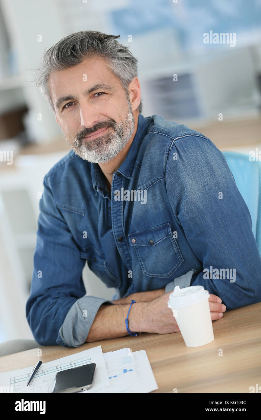 Smiling teacher sitting at desk in university office Stock Photo - Alamy