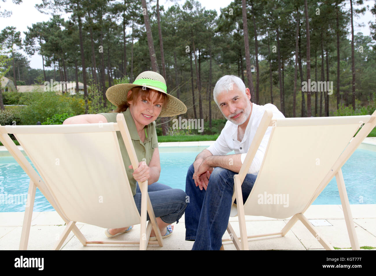 Senior couple sitting in deckchairs by a pool Stock Photo - Alamy