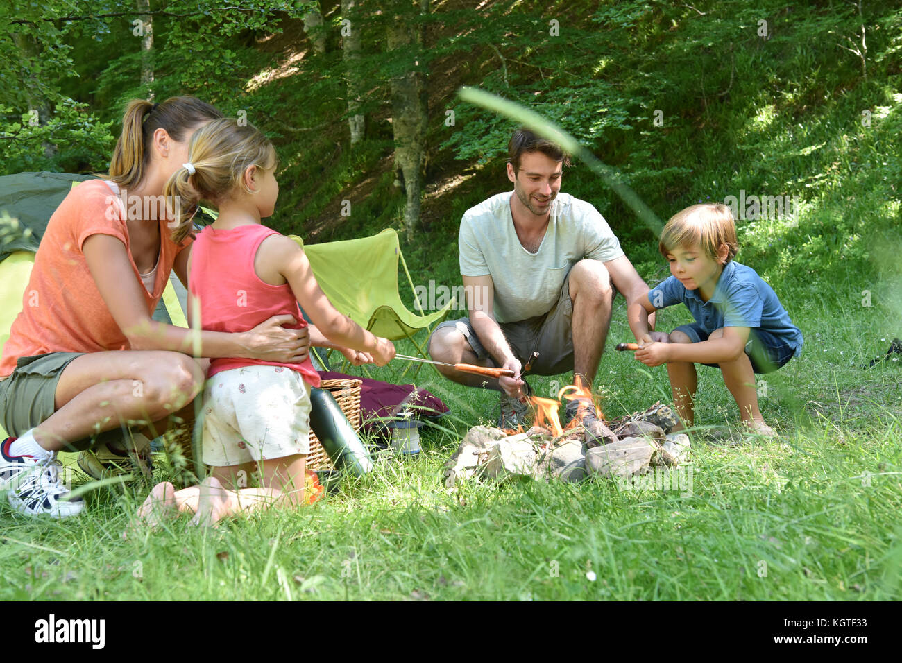 Family camping and cooking sausages in campfire Stock Photo
