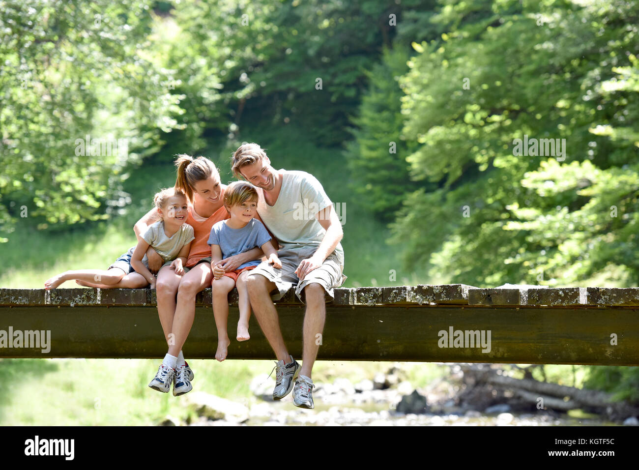 Family sitting on a bridge looking at fish in river Stock Photo - Alamy