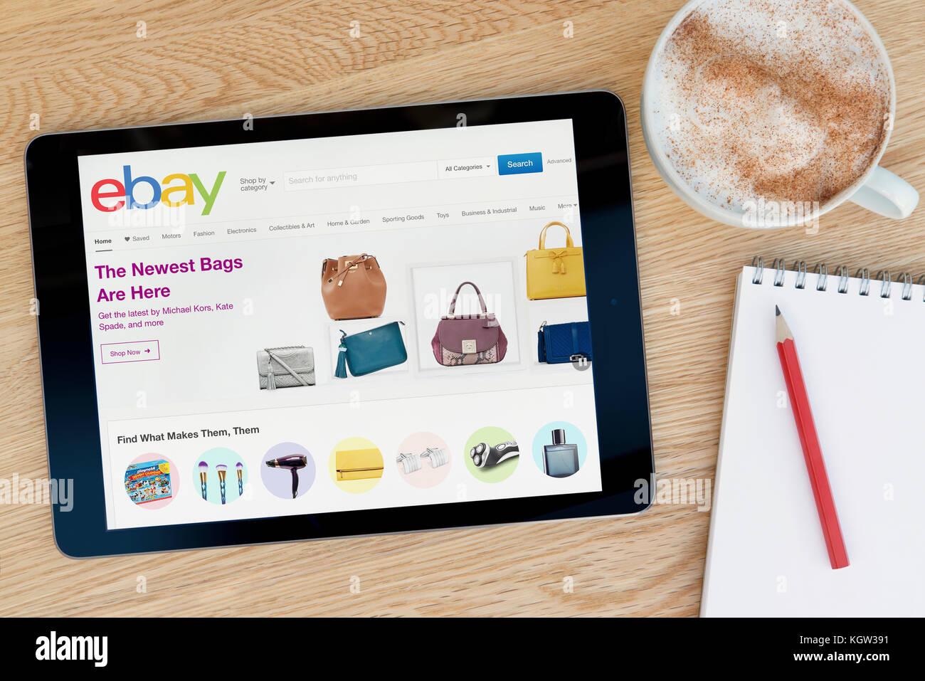 The eBay website features on an iPad tablet device which rests on a wooden table beside a notepad and pencil and a cup of coffee (Editorial use only) Stock Photo