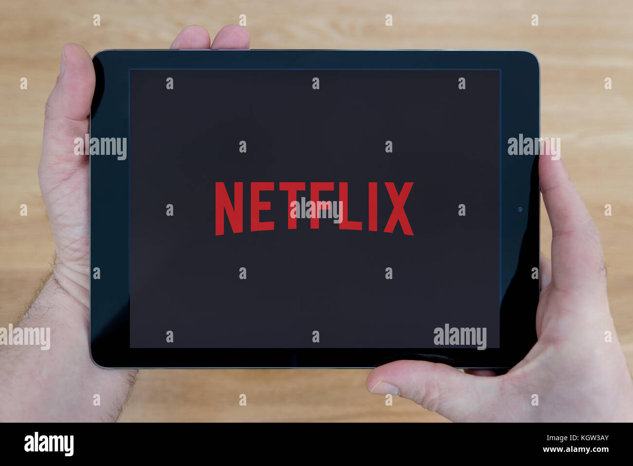 A man looks at the Netflix app on his iPad tablet device, shot against a wooden table top background (Editorial use only) Stock Photo