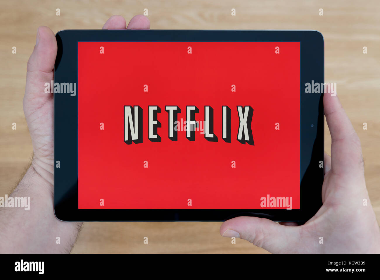 A man looks at the Netflix app on his iPad tablet device, shot against a wooden table top background (Editorial use only) Stock Photo