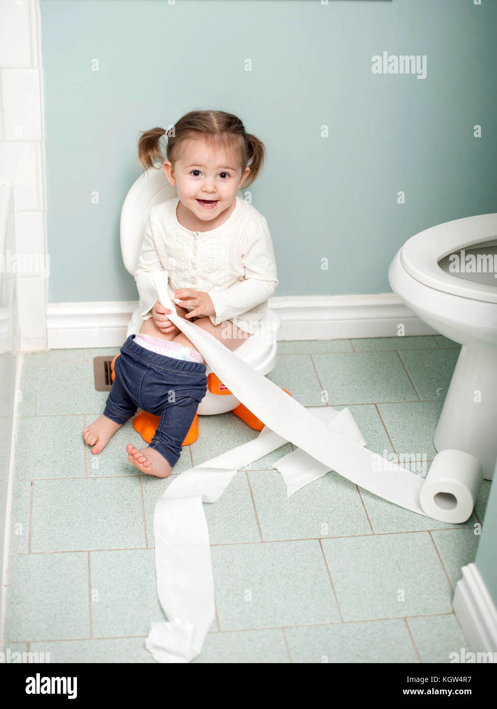 Toddler girl potty training holding toilet paper in bathroom Stock Photo