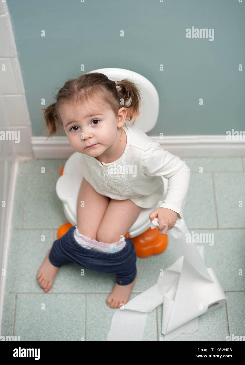 Toddler girl potty training holding toilet paper in bathroom Stock