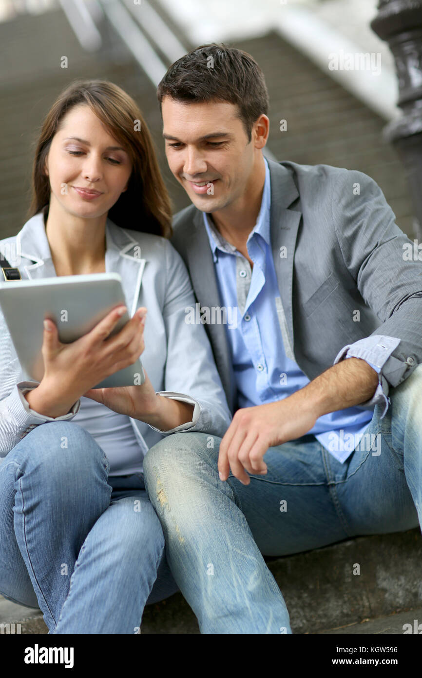 Cheerful couple sitting in stairs with electronic tablet Stock Photo