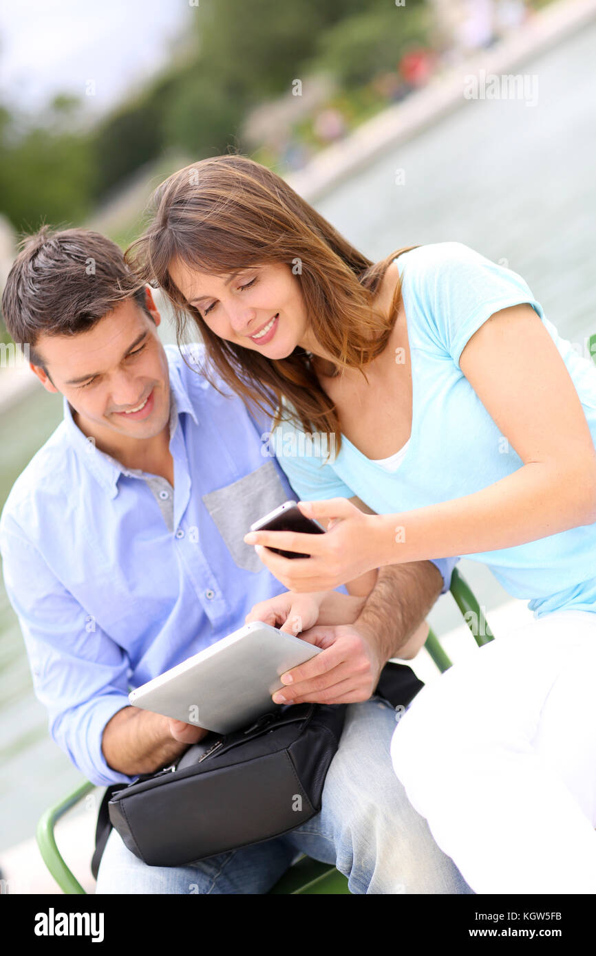 Couple using tablet and cellphone in public park Stock Photo